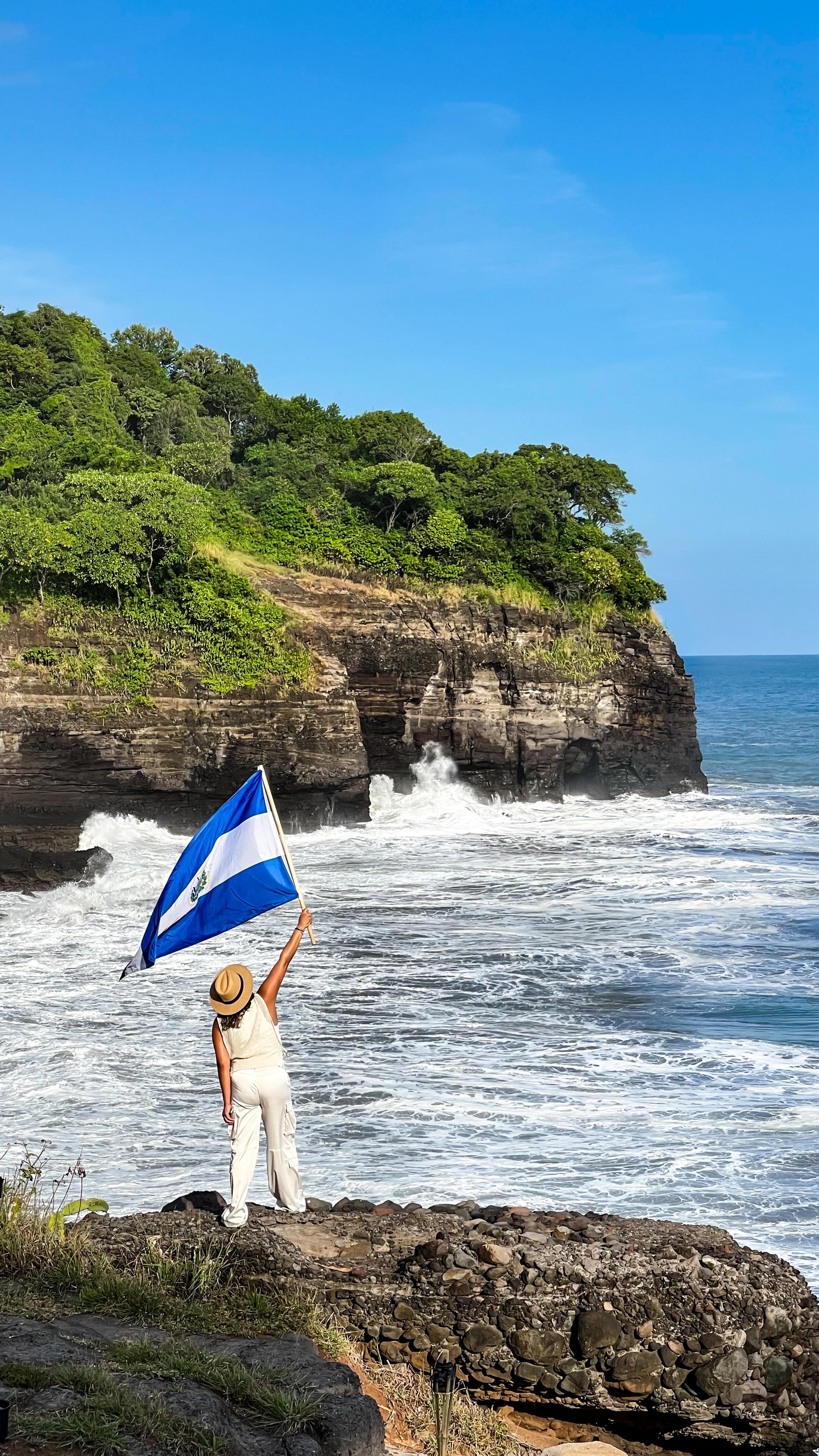 Guest holding the El Salvador flag by the coast
